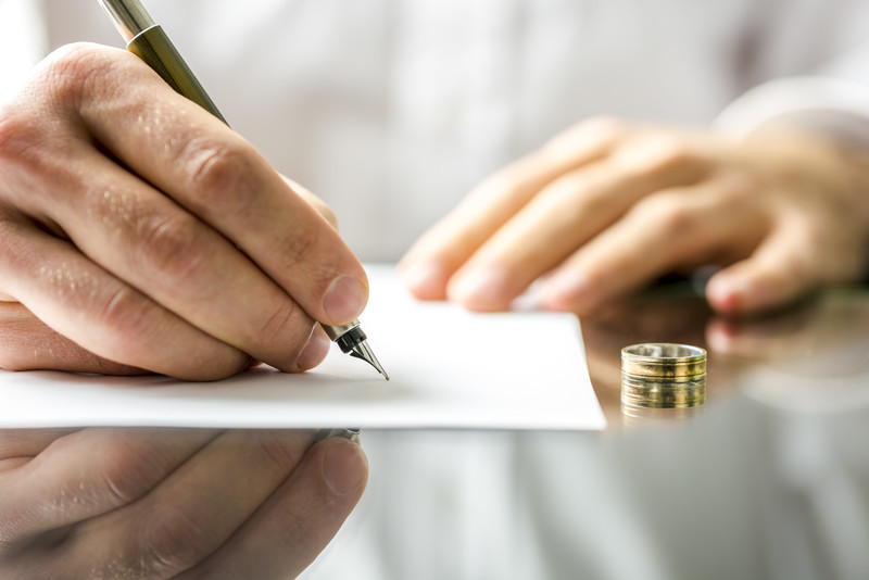 Close up of hand signing a separation agreement with wedding band on table