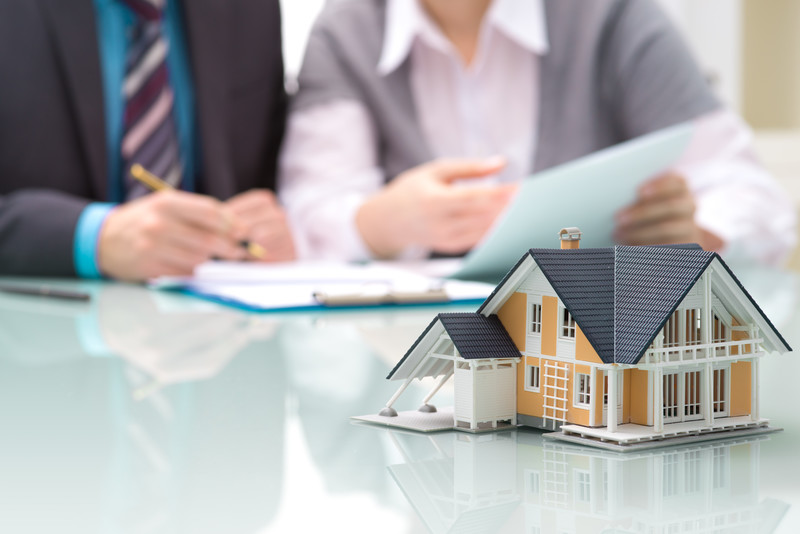 Smartly dressed man and woman looking over papers with a symbolic model house in front of them